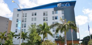 Hotel exterior with palm trees at Aloft Miami Doral.
