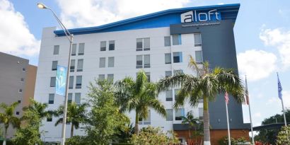 Hotel exterior with palm trees at Aloft Miami Doral.
