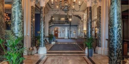 Elegant hotel lobby with marble columns and decorative chandeliers at The Grand Brighton. 