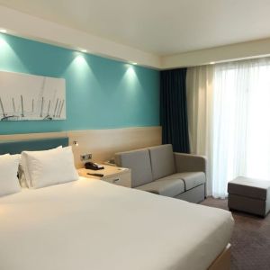 Day use room with king bed, work desk and sofa at the Hampton by Hilton London Docklands.