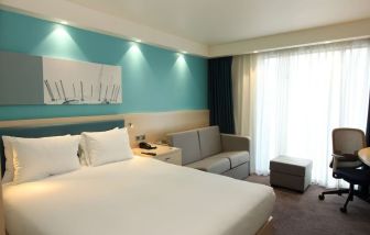 Day use room with king bed, work desk and sofa at the Hampton by Hilton London Docklands.