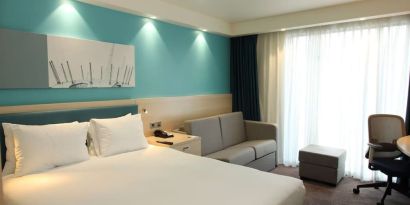 Day use room with king bed, work desk and sofa at the Hampton by Hilton London Docklands.