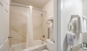 Guest bathroom with shower and tub at Coratel Plus Suites Wichita West Airport.