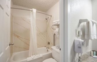 Guest bathroom with shower and tub at Coratel Plus Suites Wichita West Airport.