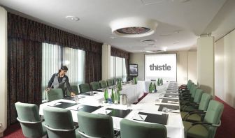 Room for business meetings with large windows, screen, and seating around single table for around a dozen people.