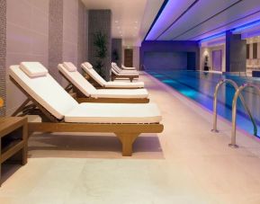 Relaxing indoor heated pool with comfortable lounge chairs at Leonardo Royal Hotel London Tower Bridge.