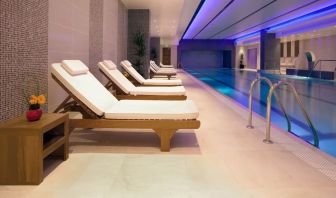 Relaxing indoor heated pool with comfortable lounge chairs at Leonardo Royal Hotel London Tower Bridge.