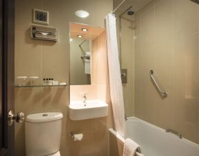 Guest bathroom with combined tub and shower at Thistle London Heathrow Terminal 5 Hotel.