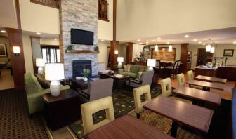 The hotel’s lounge is furnished with armchair and sofa seating around coffee tables, with a wall-mounted TV, and more tables and chairs nearby.