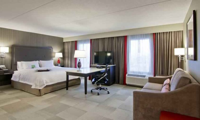 Hotel room with king size bed, sofa, TV and working station at the Hampton Inn & Suites by Hilton Toronto Markham.