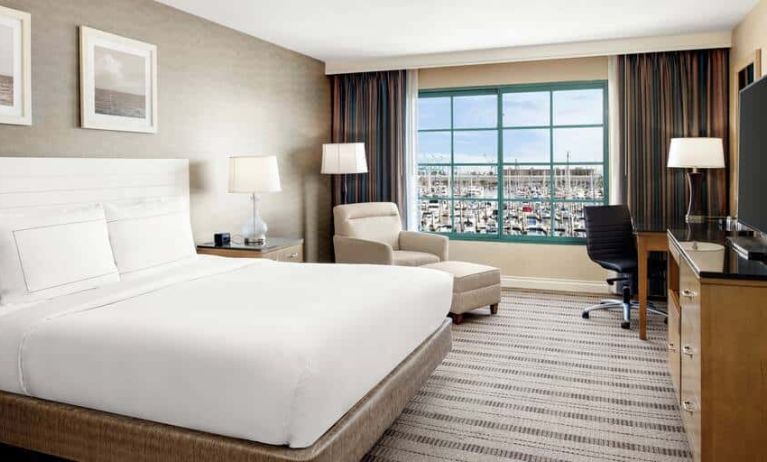 Bright queen suite hotel room with workspace and prime view of San Pedro port and marina.