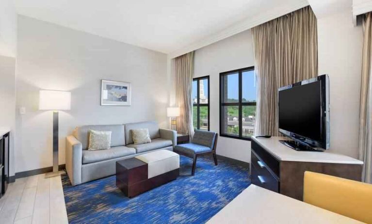 Spacious living room with desk, sofa, TV screen and windows at the Embassy Suites by Hilton Alexandria-Old Town.