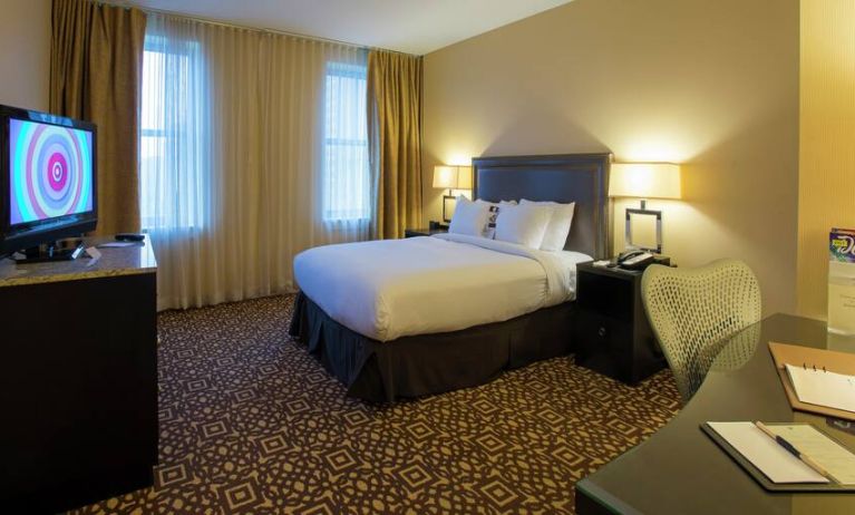 King size bed, desk and TV screen in a hotel room at the DoubleTree Suites by Hilton Detroit Downtown - Fort Shelby.