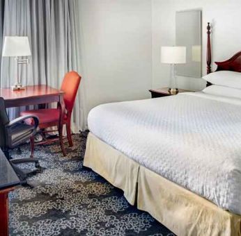 King size bed, desk and TV screen in a hotel room at the Embassy Suites by Hilton Portland-Downtown.