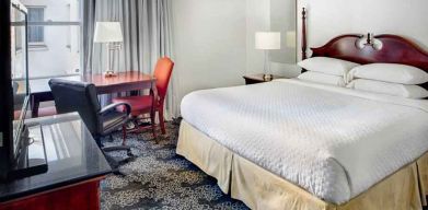 King size bed, desk and TV screen in a hotel room at the Embassy Suites by Hilton Portland-Downtown.