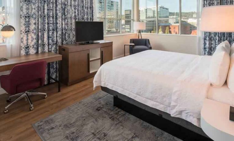 Queen size bed and working station in a hotel room at the Hampton Inn & Suites by Hilton Portland-Pearl District.