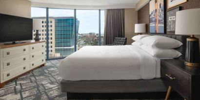 King size bed, TV screen and large window in a hotel room at the Embassy Suites by Hilton San Francisco Airport.