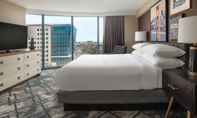 King size bed, TV screen and large window in a hotel room at the Embassy Suites by Hilton San Francisco Airport.