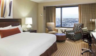 King size bed, TV screen, sofa and desk in a hotel room with window at the Hilton Omaha.