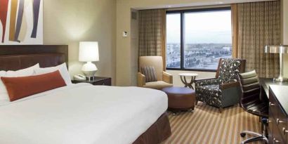 King size bed, TV screen, sofa and desk in a hotel room with window at the Hilton Omaha.