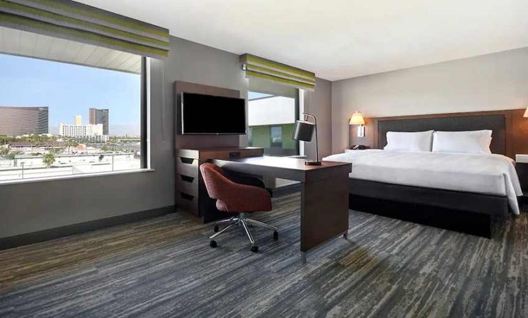 spacious king bedroom with work desk, large windows, natural light, and city views at Hampton Inn & Suites Las Vegas Convention Center.