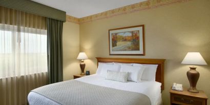 King size bed in a hotel suite with window at the Embassy Suites by Hilton Nashville - South-Cool Springs.