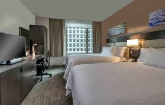 Two queen size beds, TV screen and desk in a hotel room at the Hilton Garden Inn Financial Center Manhattan Downtown, NY.