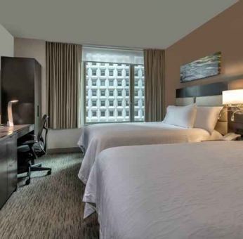 Two queen size beds, TV screen and desk in a hotel room at the Hilton Garden Inn Financial Center Manhattan Downtown, NY.