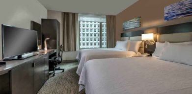 Two queen size beds, TV screen and desk in a hotel room at the Hilton Garden Inn Financial Center Manhattan Downtown, NY.