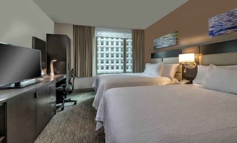 Two queen size beds, TV screen and desk in a hotel room at the Hilton Garden Inn Financial Center Manhattan Downtown, NY.