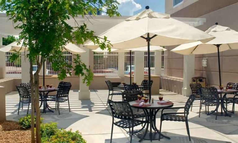 Beautiful outdoor patio with chairs, tables and sun umbrellas at the Hilton Garden Inn Albuquerque Uptown.