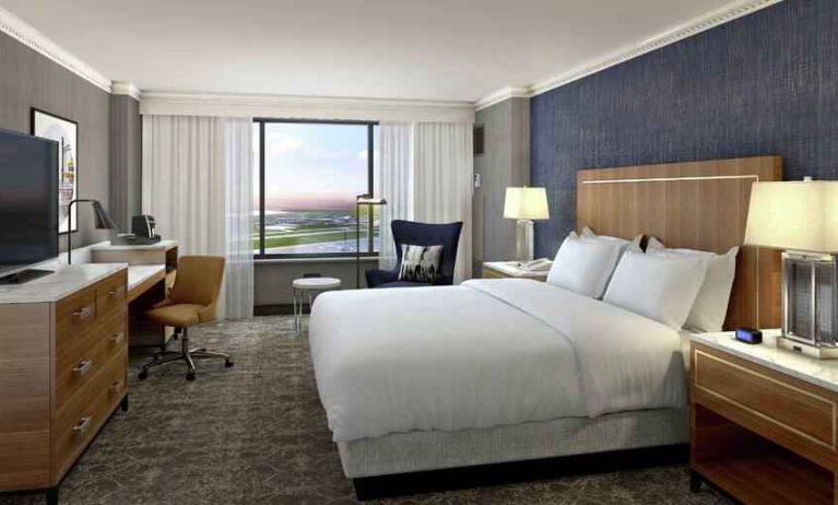 King size bed, TV screen and desk in a hotel guestroom at the Hilton New Orleans Airport.