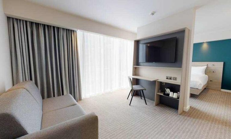 Living room with sofa, TV screen and desk at the Hampton by Hilton Manchester Northern Quarter.