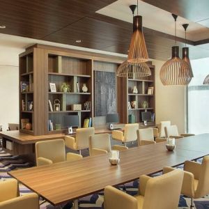 Bronze eclectic lighting hangs over long wooden table lined with floor to ceiling bookshelves.