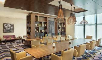 Bronze eclectic lighting hangs over long wooden table lined with floor to ceiling bookshelves.