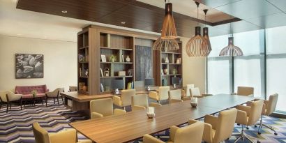 Bronze eclectic lighting hangs over long wooden table lined with floor to ceiling bookshelves.