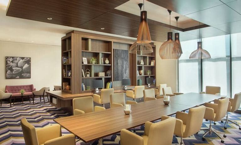 Bronze eclectic lighting hangs over long wooden table lined with floor to ceiling bookshelves.