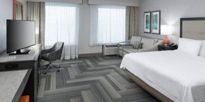 1 king bed room with snack bar, tv, desk and couch at the Hampton Suites Atlanta Perimeter Dunwoody