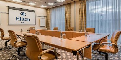 Long u-shaped light brown wooden table with seating for 8-10 guests.