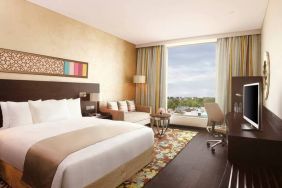 Spacious executive day room with floor-to-ceiling window, large desk, television, king bed at the Hilton Jaipur.