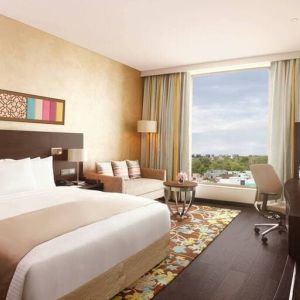 Spacious executive day room with floor-to-ceiling window, large desk, television, king bed at the Hilton Jaipur.