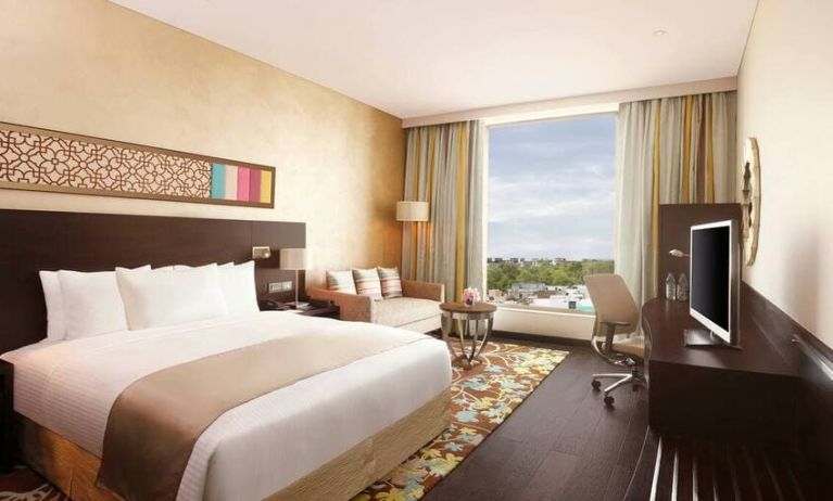 Spacious executive day room with floor-to-ceiling window, large desk, television, king bed at the Hilton Jaipur.