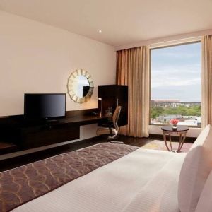 Bright king guest room with view out into Jaipur, India, complete with sitting area and long desk with television and workspace.