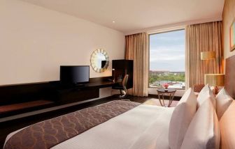 Bright king guest room with view out into Jaipur, India, complete with sitting area and long desk with television and workspace.