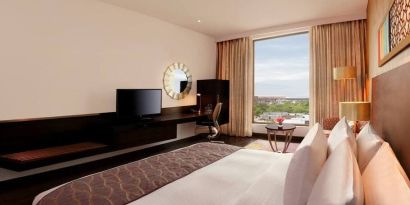 Bright king guest room with view out into Jaipur, India, complete with sitting area and long desk with television and workspace.