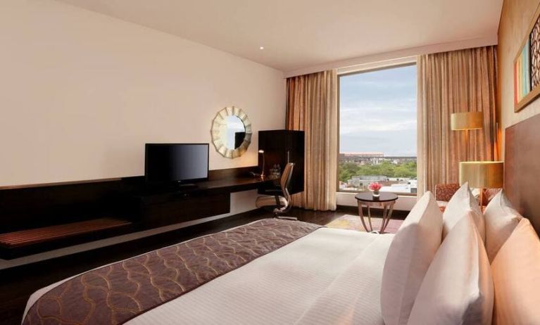 Bright king guest room with view out into Jaipur, India, complete with sitting area and long desk with television and workspace.