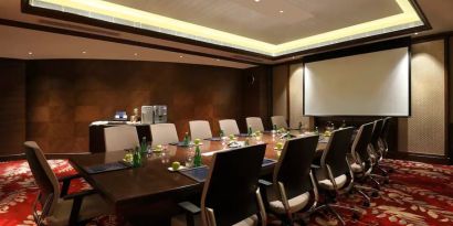 Sleek boardroom with large projection screen, seating for up to 12-15 people.