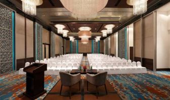 Long presentation and banquet hall with ornate chandeliers, a podium and sitting area for two panelists at the front, at the Hilton Jaipur, India.