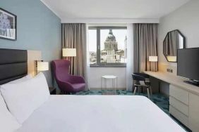 lovely kind bedroom with TV, workspace, couch, and city views at Hilton Garden Inn Budapest City Centre.