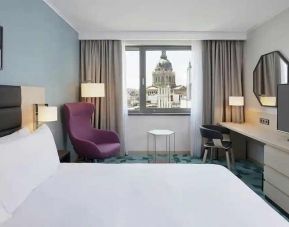 lovely kind bedroom with TV, workspace, couch, and city views at Hilton Garden Inn Budapest City Centre.